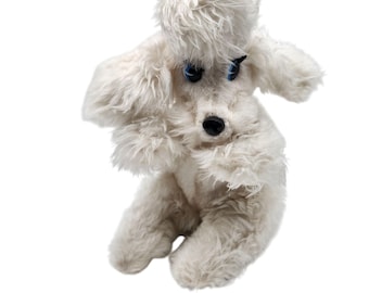 May include: A white plush poodle toy with blue eyes and a black nose. The poodle has a fluffy, textured coat and is posed in a playful stance. The toy is set against a white background.