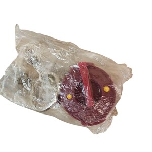 May include: A new, unopened kitchen appliance, possibly a blender or food processor component, is encased in clear plastic. The item features a deep red lid with a red handle and two yellow accents. The item is on a white background.