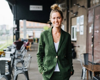 Könnte beinhalten: Ein dunkelgrüner Blazer und eine passende Hose aus Leinen, getragen über einem schlichten weißen T-Shirt mit V-Ausschnitt. Der Blazer hat einen Knopfverschluss und ein Revers, während die Hose eine lockere Passform mit umgeschlagenen Säumen hat.