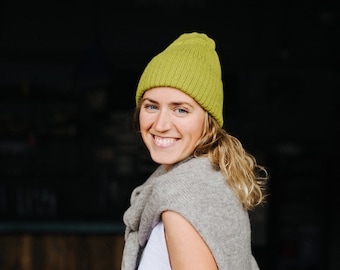 Puede incluir: Una mujer con el pelo largo y rubio lleva una camisa blanca, un cárdigan gris y una boina verde brillante. Está sonriendo y mirando a la cámara.