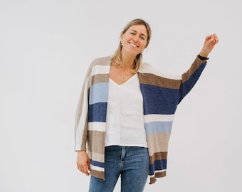 May include: A woman wearing a striped cardigan with blue, brown and white stripes, a white v-neck shirt, blue jeans and brown leather clogs.