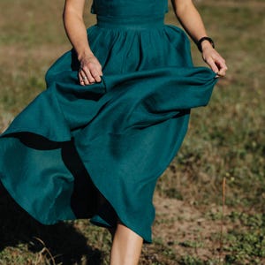 Peut inclure: Une robe deux pi&egrave;ces de couleur teal, compos&eacute;e d'un haut sans manches et d'une jupe ample. La jupe est fronc&eacute;e &agrave; la taille, cr&eacute;ant une silhouette ample. La robe est faite d'un tissu doux et fluide. La personne marche dans un champ herbeux.