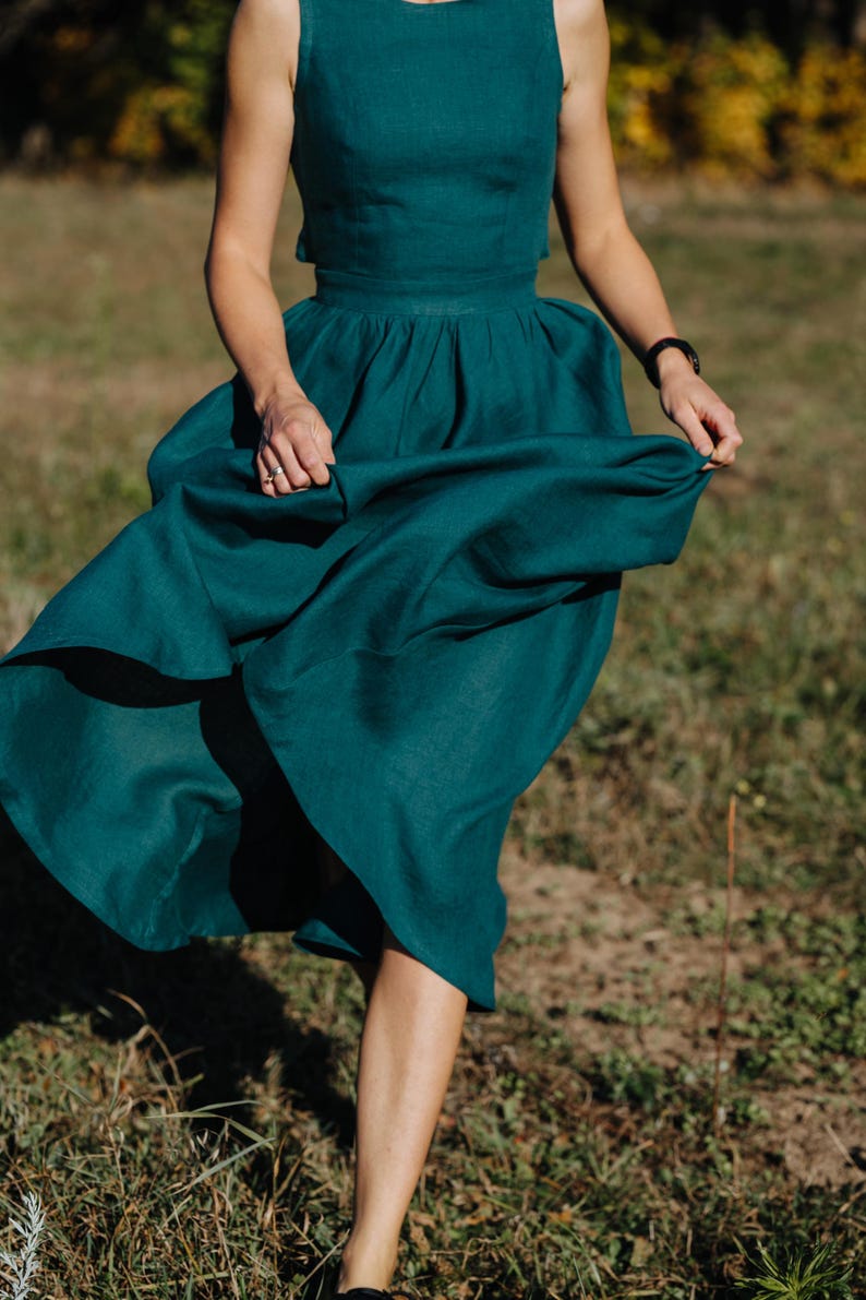 Peut inclure: Une robe deux pi&egrave;ces de couleur teal, compos&eacute;e d'un haut sans manches et d'une jupe ample. La jupe est fronc&eacute;e &agrave; la taille, cr&eacute;ant une silhouette ample. La robe est faite d'un tissu doux et fluide. La personne marche dans un champ herbeux.