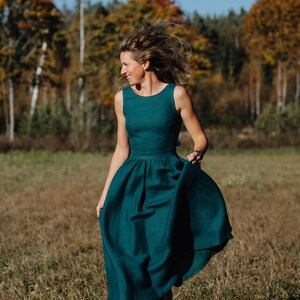 Peut inclure: Une robe sans manches de couleur sarcelle avec une jupe &eacute;vas&eacute;e. La robe est faite d'un tissu doux et a un corsage ajust&eacute;. La personne marche dans un champ avec des arbres en arri&egrave;re-plan.
