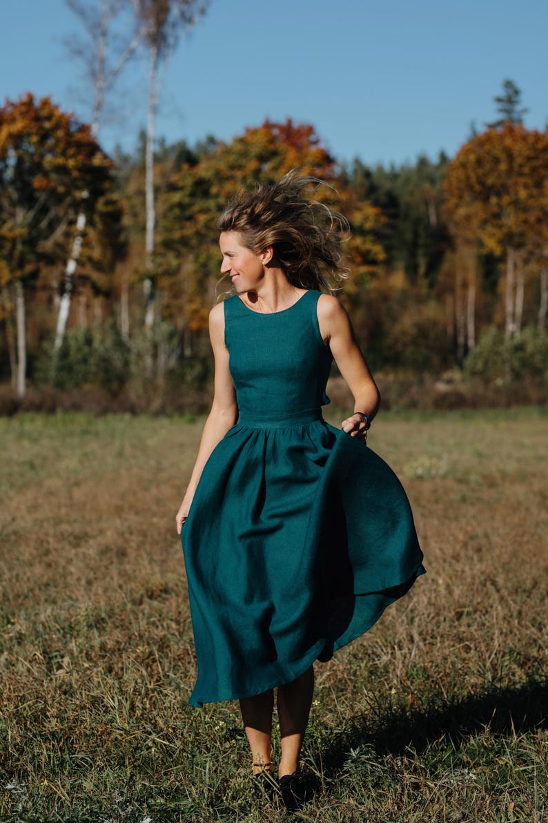 Peut inclure: Une robe sans manches de couleur sarcelle avec une jupe &eacute;vas&eacute;e. La robe est faite d'un tissu doux et a un corsage ajust&eacute;. La personne marche dans un champ avec des arbres en arri&egrave;re-plan.