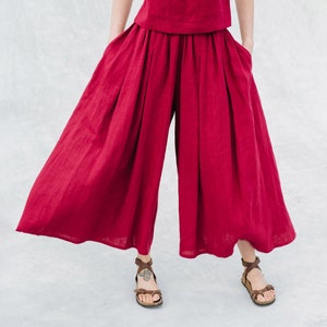 May include: A woman is wearing a red linen top and wide-leg pants. The outfit is a matching set. The pants have a wide, flowing silhouette.