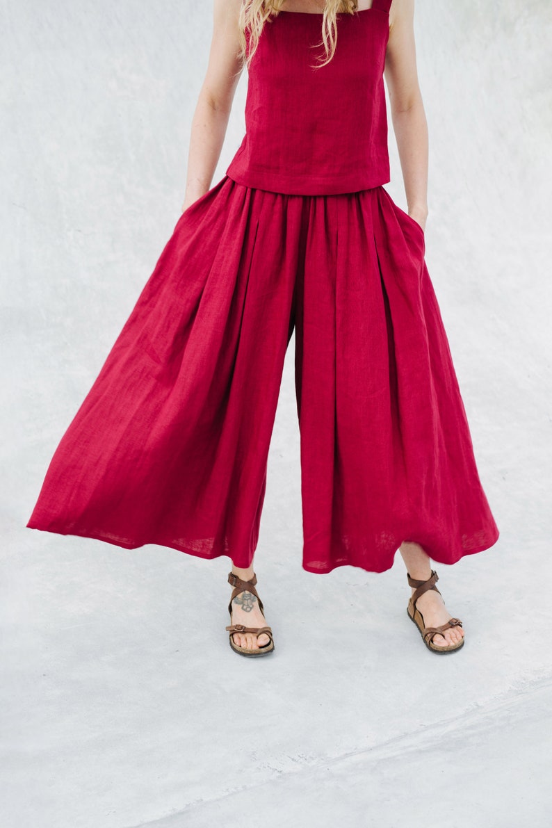 May include: A woman is wearing a red linen top and wide-leg pants. The outfit is a matching set. The pants have a wide, flowing silhouette.