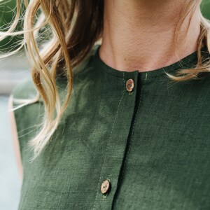May include: A close-up of a green linen shirt with wooden buttons. The shirt has a simple, classic design and is perfect for a casual summer outfit.