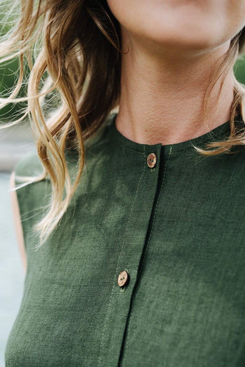 May include: A close-up of a green linen shirt with wooden buttons. The shirt has a simple, classic design and is perfect for a casual summer outfit.