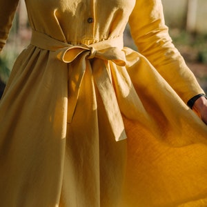 Pode incluir: Um vestido de linho amarelo de manga comprida com um la&ccedil;o na cintura.