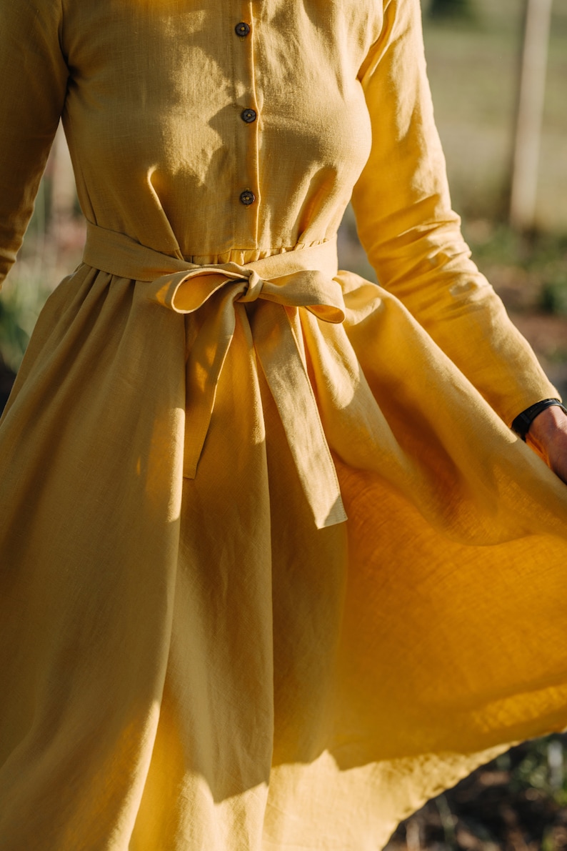 Pode incluir: Um vestido de linho amarelo de manga comprida com um la&ccedil;o na cintura.