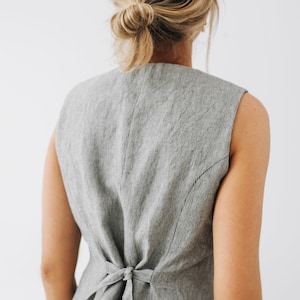 May include: A gray linen vest with a tie back detail. The vest is sleeveless and has a striped pattern.