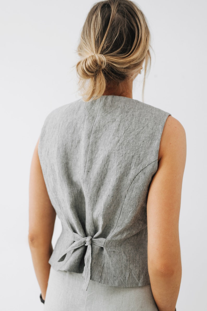 May include: A gray linen vest with a tie back detail. The vest is sleeveless and has a striped pattern.