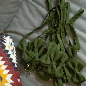 K&ouml;nnte beinhalten: Ein Stapel gr&uuml;ner Fliegen aus Stoff. Die Fliegen sind in einem Stapel angeordnet, wobei die B&auml;nder der Fliegen sichtbar sind.