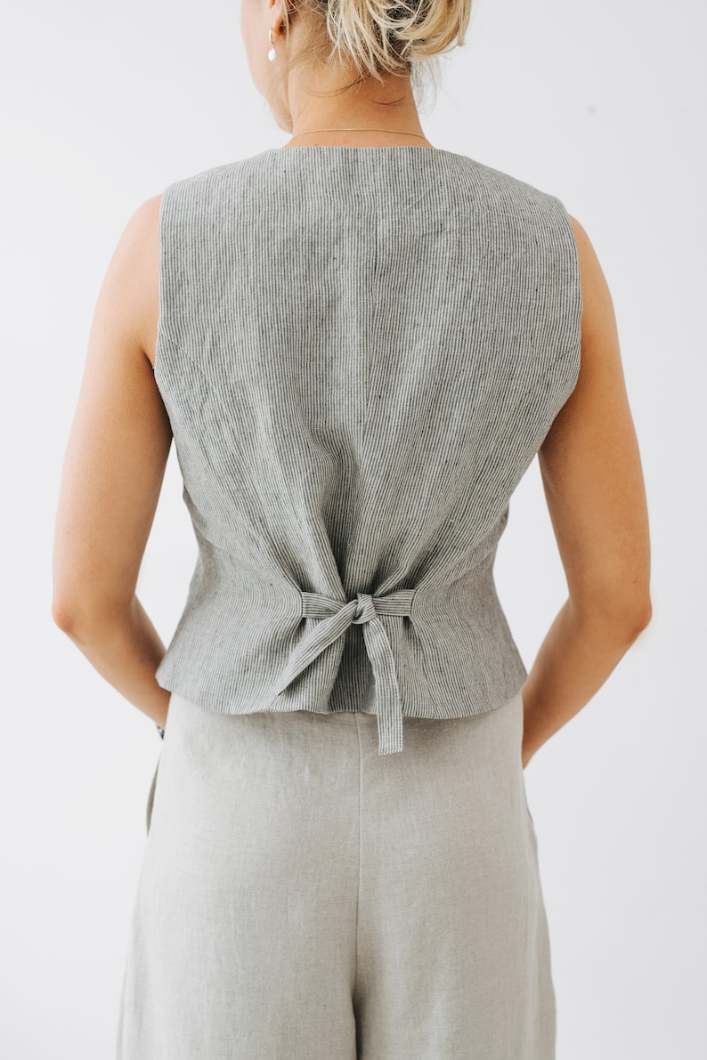 May include: A gray linen vest with thin black stripes. The vest has a tie closure in the back.