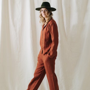 Puede incluir: Una persona lleva un pantal&oacute;n de lino de color &oacute;xido con un sombrero verde de ala ancha. La persona est&aacute; de pie sobre un fondo blanco.