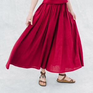 May include: A woman wearing a burgundy linen top and skirt. The skirt is flowing and has a gathered waist. She is wearing brown sandals.
