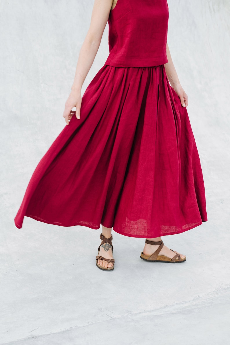 May include: A woman wearing a burgundy linen top and skirt. The skirt is flowing and has a gathered waist. She is wearing brown sandals.