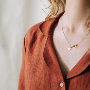 Puede incluir: Primer plano de una persona que lleva una camisa de lino de color &oacute;xido con cuello abotonado. La persona lleva un collar de oro con un dije de coraz&oacute;n y una letra.