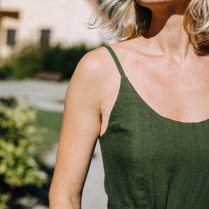 K&ouml;nnte beinhalten: Eine Frau tr&auml;gt ein dunkelgr&uuml;nes Leinen-Sommerkleid mit d&uuml;nnen Tr&auml;gern. Das Kleid hat eine taillierte Taille mit einem passenden Stoffg&uuml;rtel.
