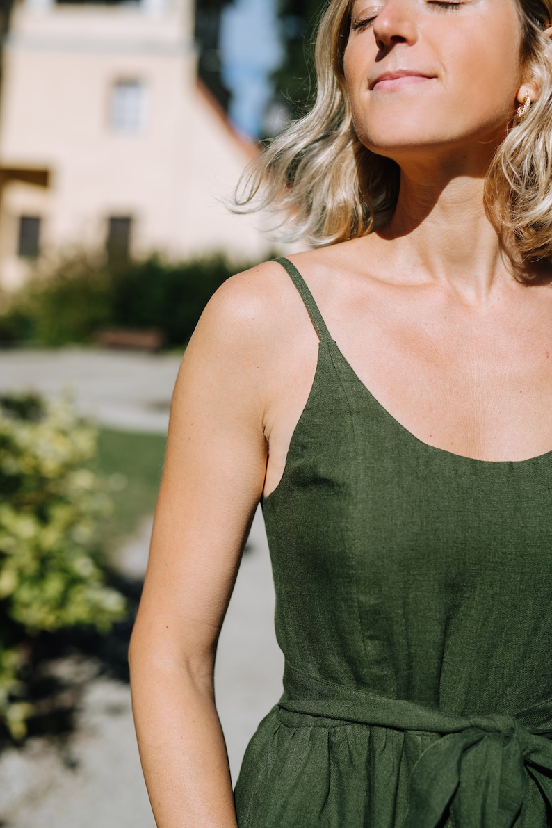 K&ouml;nnte beinhalten: Eine Frau tr&auml;gt ein dunkelgr&uuml;nes Leinen-Sommerkleid mit d&uuml;nnen Tr&auml;gern. Das Kleid hat eine taillierte Taille mit einem passenden Stoffg&uuml;rtel.