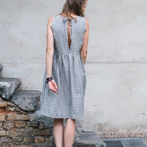 May include: A woman wearing a gray linen dress with a low back and a tie detail. She is standing on a set of stone steps.