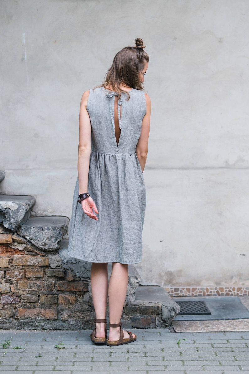 May include: A woman wearing a gray linen dress with a low back and a tie detail. She is standing on a set of stone steps.