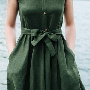 May include: A dark green linen dress with a button-up front and a tie belt. The dress has a relaxed fit and a slightly flared skirt.