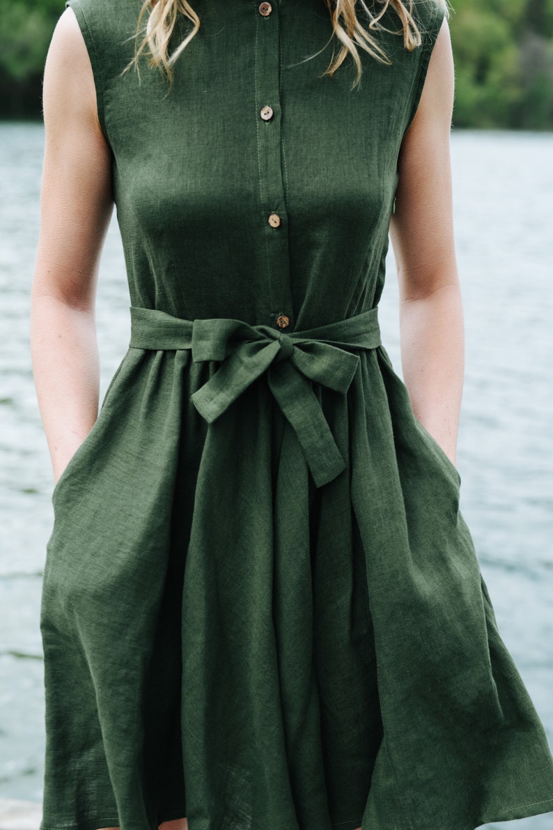 May include: A dark green linen dress with a button-up front and a tie belt. The dress has a relaxed fit and a slightly flared skirt.