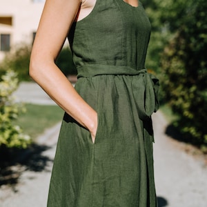 K&ouml;nnte beinhalten: Ein dunkelgr&uuml;nes Leinenkleid mit Bindeg&uuml;rtel und Taschen. Das Kleid ist &auml;rmellos und hat einen runden Ausschnitt.