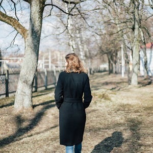 May include: A woman wearing a black coat and blue jeans walks through a park with bare trees.