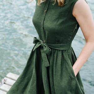 May include: A dark green linen dress with a button-up front, a tie belt, and pockets. The dress has a fitted bodice and a flowy skirt.