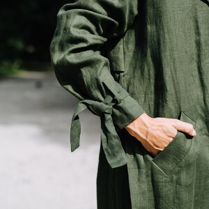 May include: A dark green linen jacket with a tie detail on the sleeves and a pocket on the front.