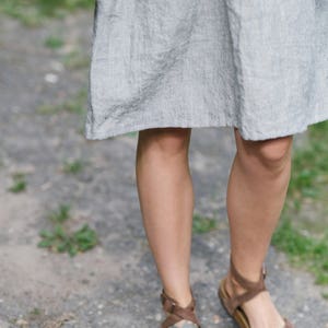 May include: A pair of brown leather sandals with straps and buckles. The sandals have a cork footbed and are worn by a person with red nail polish.