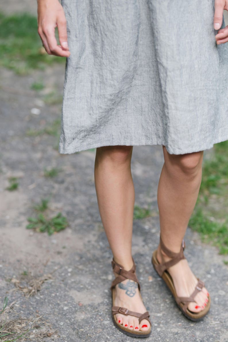 May include: A pair of brown leather sandals with straps and buckles. The sandals have a cork footbed and are worn by a person with red nail polish.