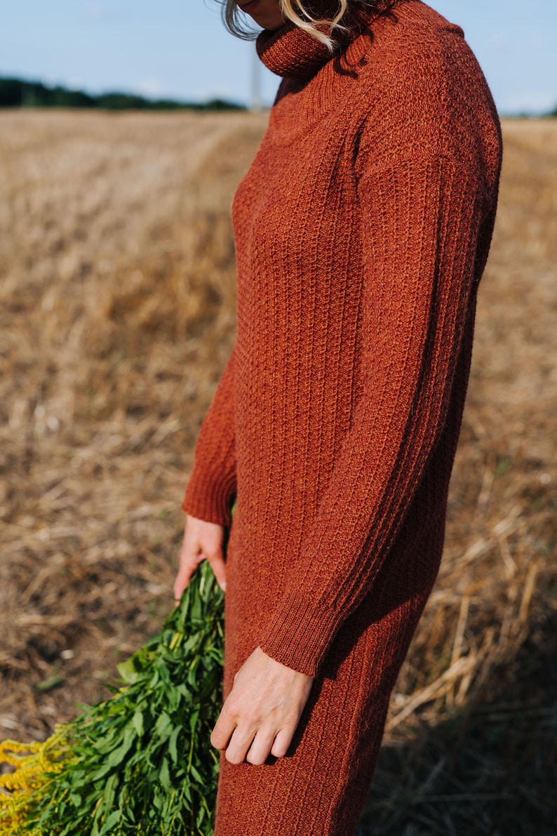 May include: A rust-coloured turtleneck sweater dress with a ribbed texture. The dress is being worn by a person holding a bouquet of green flowers.