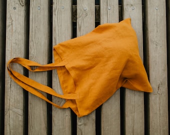 May include: A mustard yellow tote bag made of linen fabric with a single strap. The bag is lying on a wooden surface.