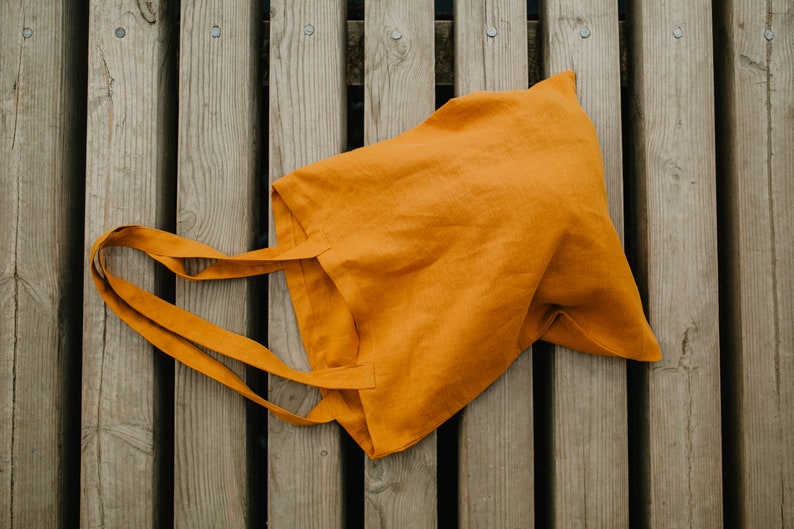 May include: A mustard yellow tote bag made of linen fabric with two handles.