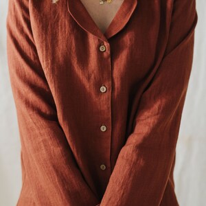 Puede incluir: Una camisa de lino de color &oacute;xido con cuello y cierre de botones. La camisa tiene mangas largas y un corte holgado.