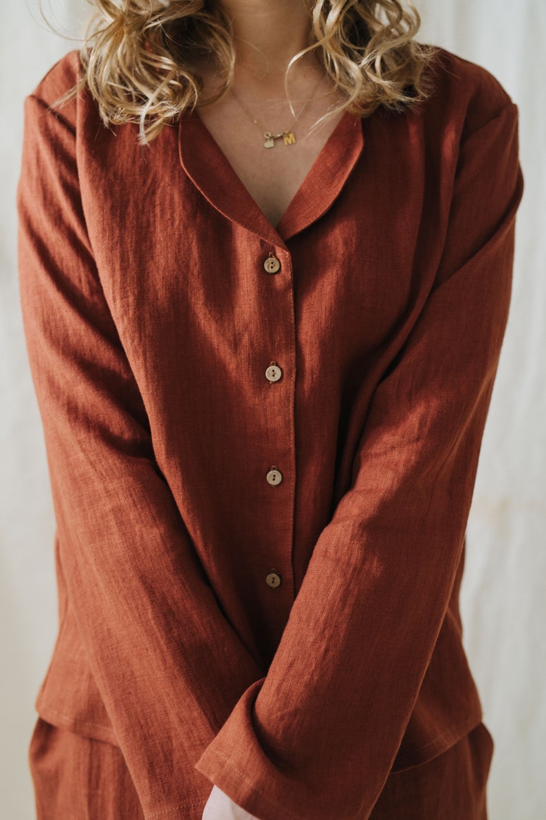 Puede incluir: Una camisa de lino de color &oacute;xido con cuello y cierre de botones. La camisa tiene mangas largas y un corte holgado.