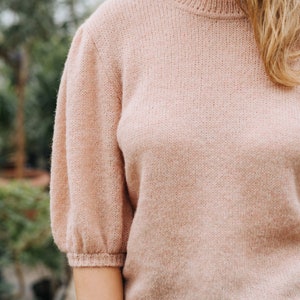 May include: A soft, pale pink knitted sweater with a round neckline and slightly puffed sleeves.