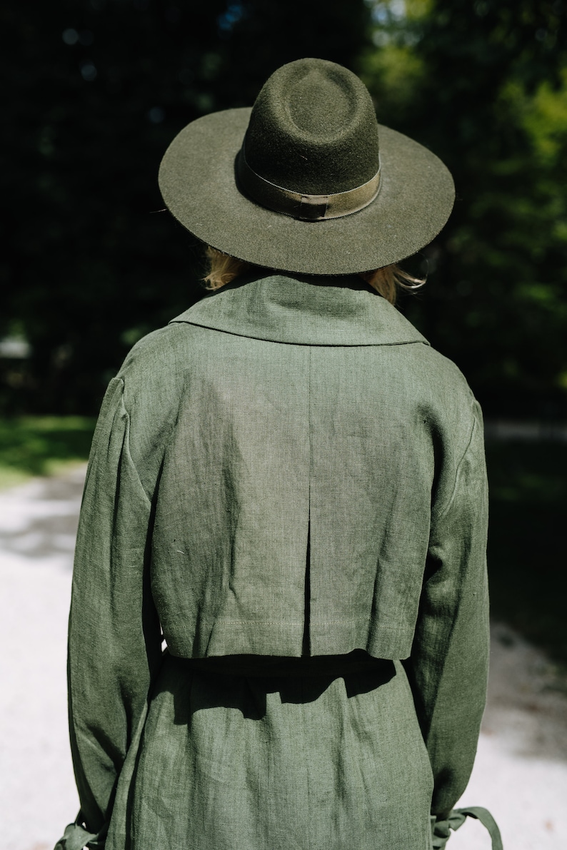 May include: A person wearing a green linen trench coat with a wide brimmed green felt hat.