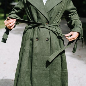 May include: A long, green linen trench coat with a double-breasted closure and a self-tie belt. The coat has a relaxed fit and a slightly flared skirt.