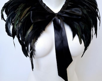 May include: A black feather collar with a black satin ribbon tied in a bow. The collar is worn on a white mannequin.