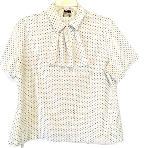 Pode incluir: Blusa branca de manga curta com colarinho franzido e bolinhas pretas e vermelhas.