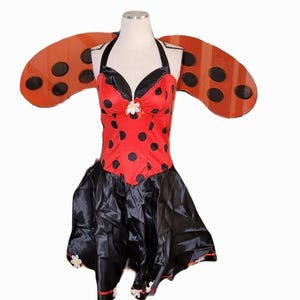 以下が含まれることがあります： 黒い水玉模様の赤いボディスと黒いスカートが特徴のてんとう虫のコスチューム。コスチュームには、黒い斑点のあるオレンジ色の翼が含まれています。白い花がネックラインにあります。