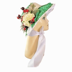 May include: A decorative hat with a green patterned brim and a cream-colored crown. The hat is adorned with cream-colored roses, red berries, and greenery. A white ribbon is tied around the neck of the mannequin.