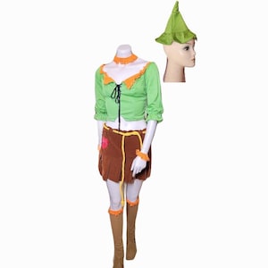Pode incluir: Um conjunto de fantasia verde e marrom, incluindo um top verde com acabamentos laranja, uma saia marrom e botas a condizer. Um chapéu verde também está incluído. A fantasia é exibida em um manequim.