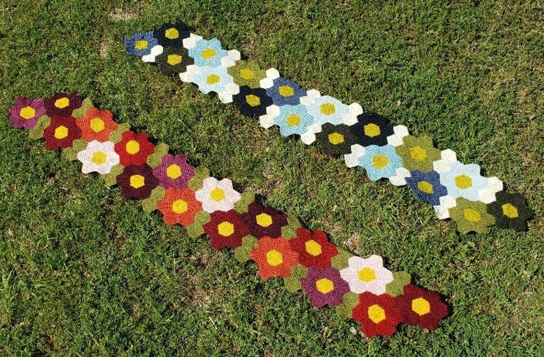 May include: Two crocheted flower-shaped rugs in different colour combinations. The top rug is made with green, blue, and white yarn. The bottom rug is made with red, orange, yellow, and purple yarn.