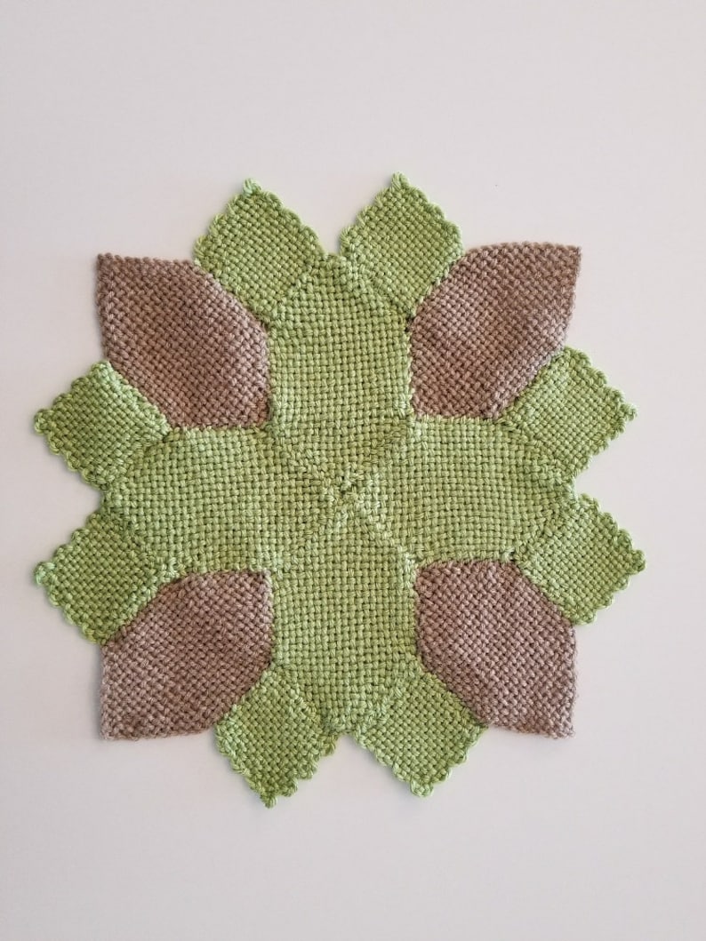 May include: A square knitted coaster with a geometric design. The coaster is made of two colours of yarn: green and brown. The design features eight points, with each point alternating between the two colours.